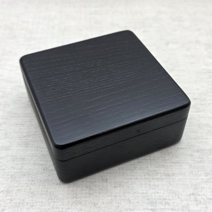 Closed black painted ash wood gift box showing sleek rounded corners and natural wood grain texture under light, modern minimalist design.