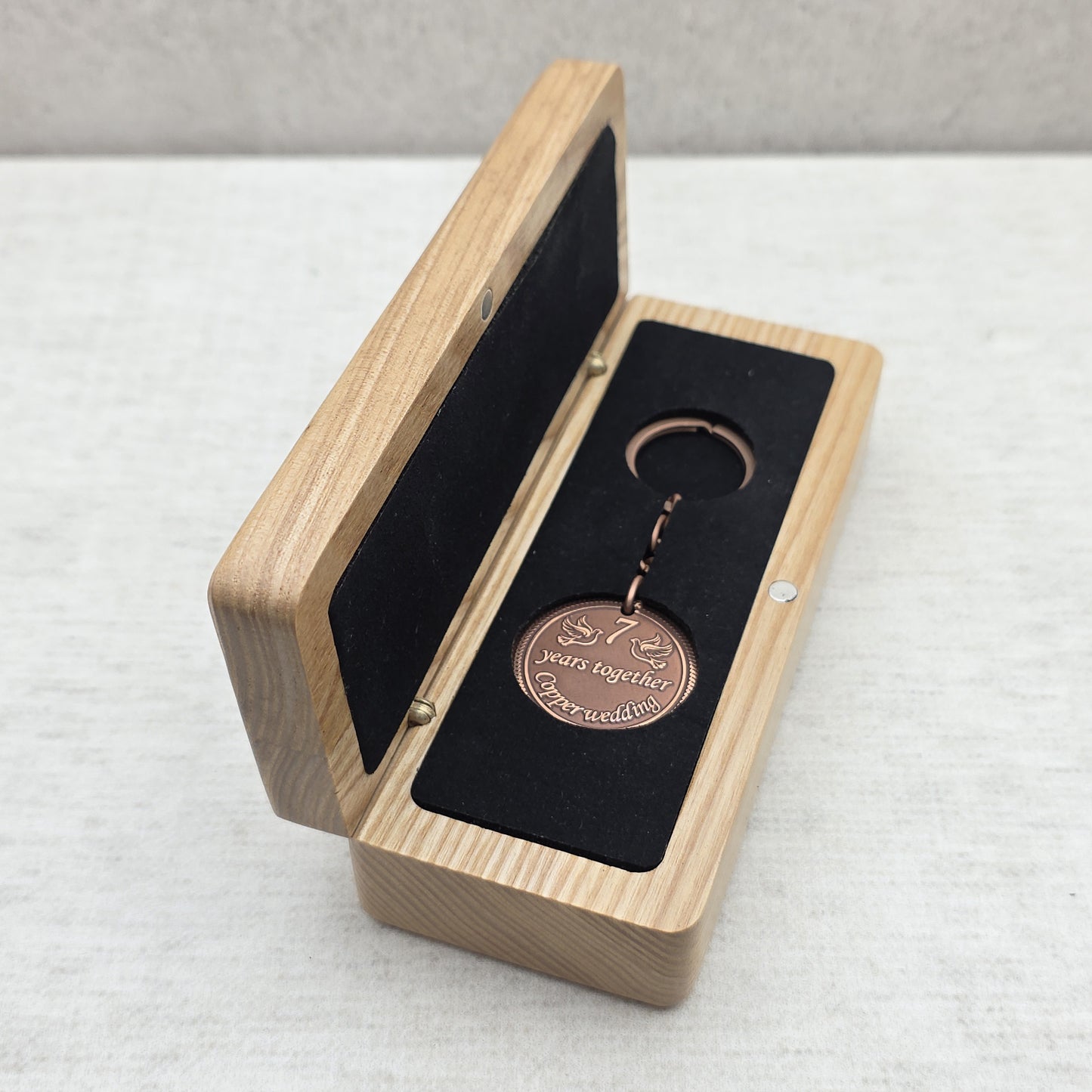 Open solid ash wood gift box with personalized coin keychain placed inside black velvet insert