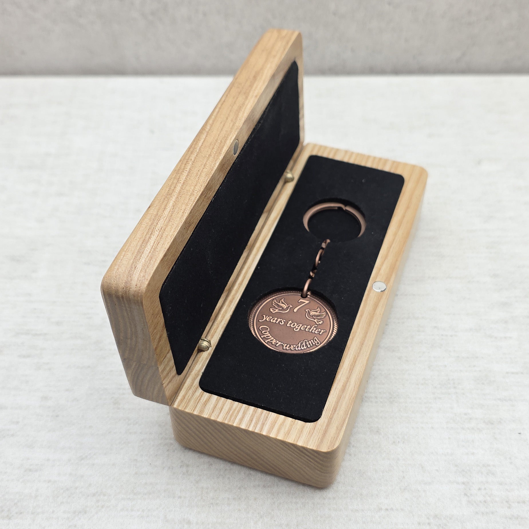 Open solid ash wood gift box with personalized coin keychain placed inside black velvet insert