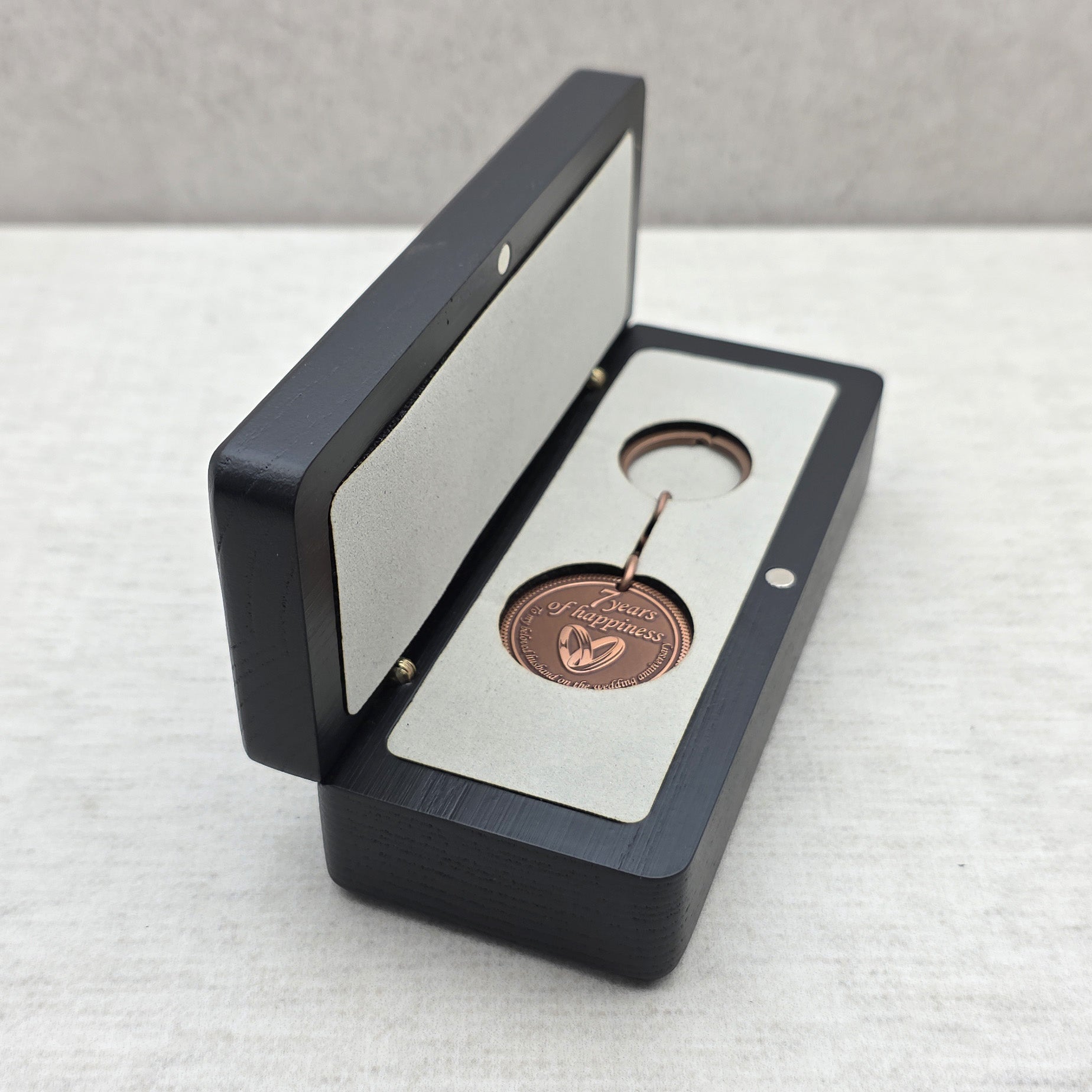 Open black ash wood gift box with personalized keychain placed inside light gray velvet insert
