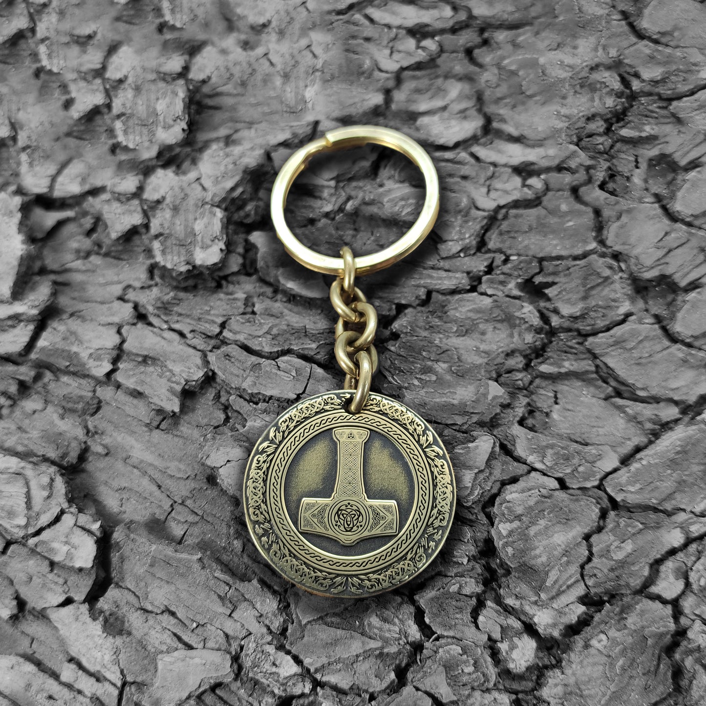 Personalized brass Thor's Hammer keychain on a rustic dark wood bark texture, highlighting the antique finish and durable metal quality of the talisman.