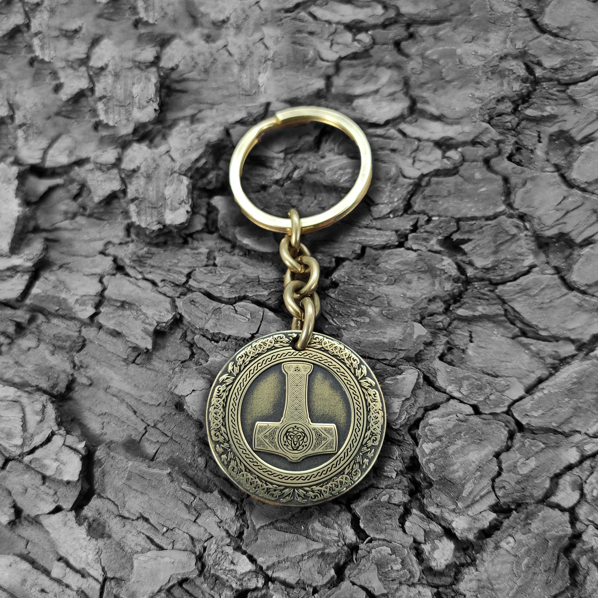 Personalized brass Thor's Hammer keychain on a rustic dark wood bark texture, highlighting the antique finish and durable metal quality of the talisman.