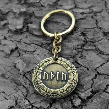 Brass rune keychain on a rustic dark wood bark texture, showcasing the antique finish and durable metal quality of the personalized talisman.