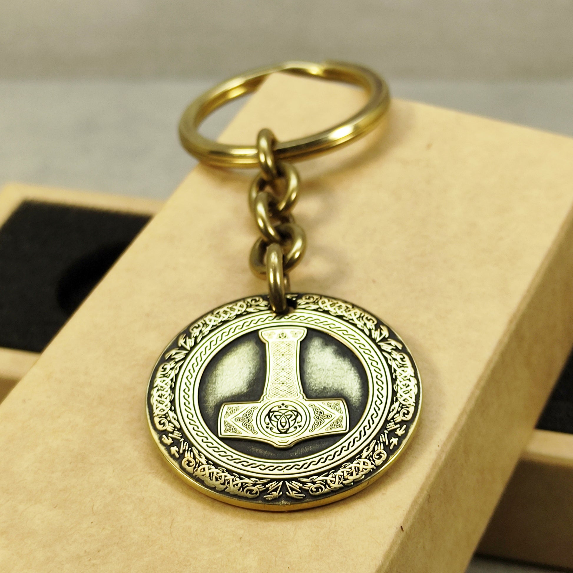 Close-up of a brass Thor's Hammer coin keychain with deep laser engraving, antique patina finish, and decorative border on a craft gift box.
