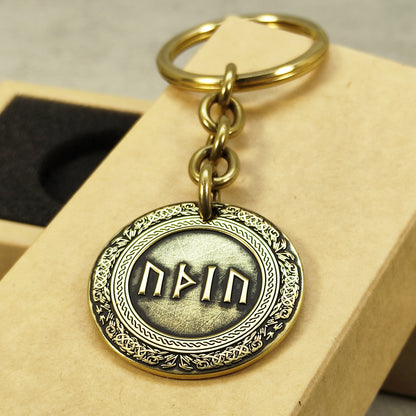 Close-up of a brass rune coin keychain with deep laser engraving, antique patina finish, and decorative border on a craft gift box.