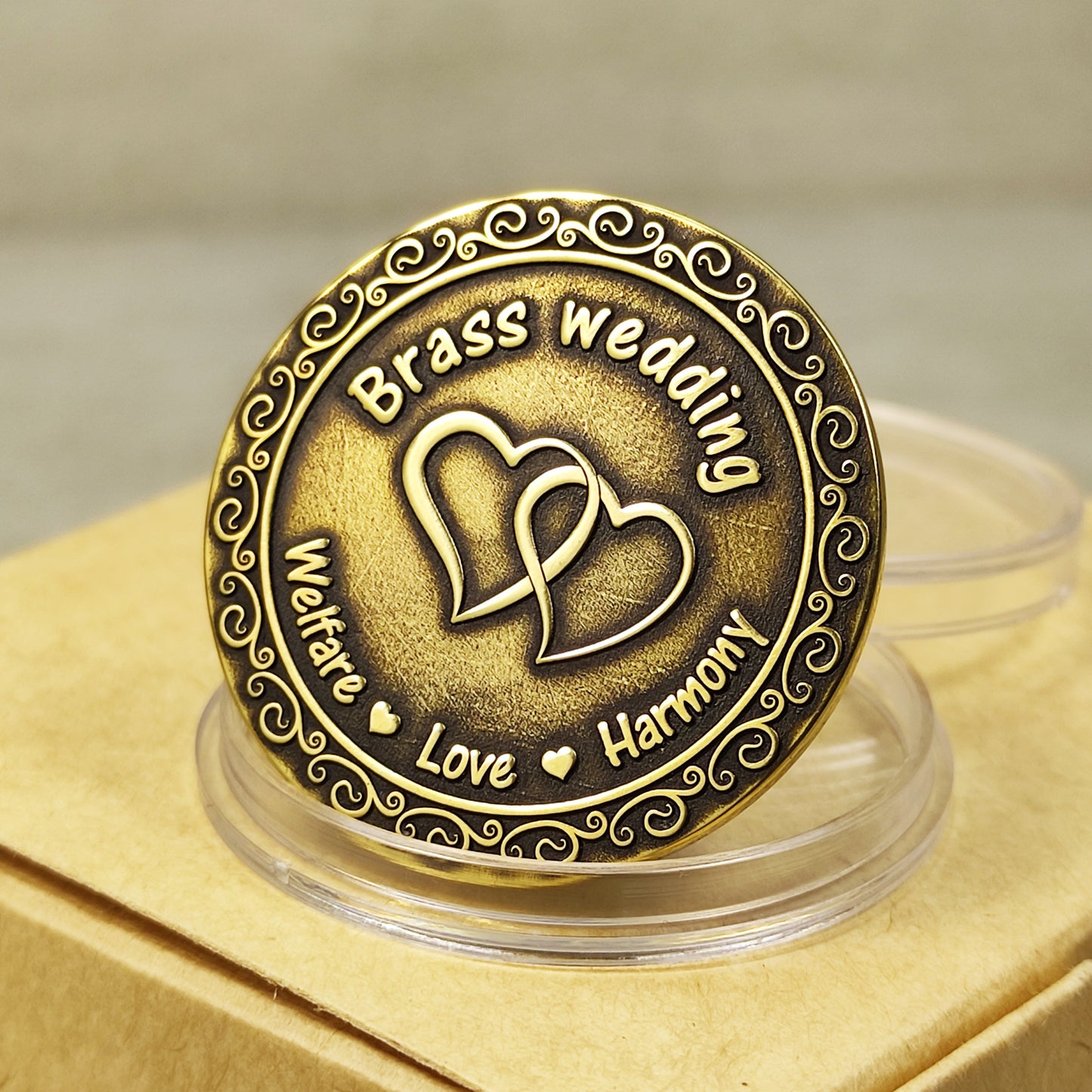 Close-up of personalized brass wedding anniversary coin with vintage patina, featuring intertwined hearts and "Welfare Love Harmony" engraving.