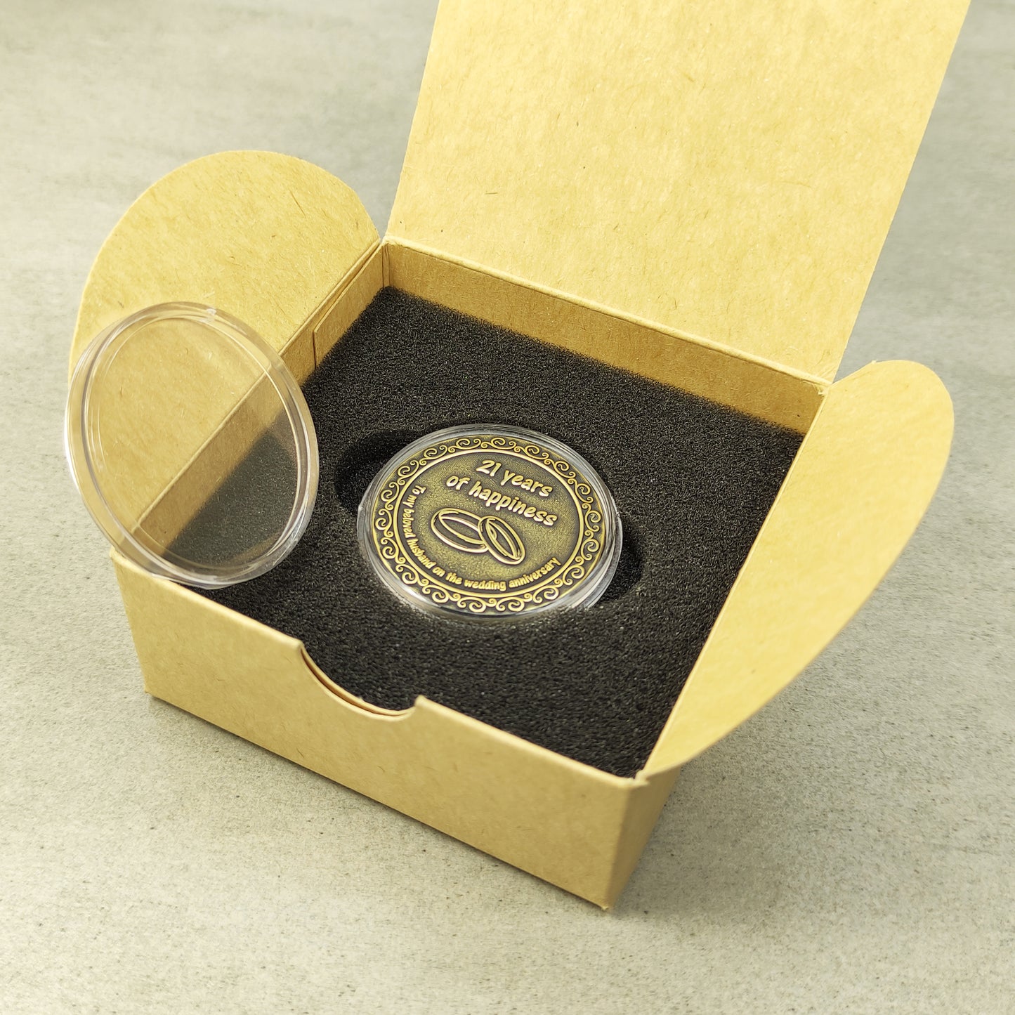 Personalized brass metal coin in a clear acrylic case next to a minimalist eco-friendly gift box for a wedding anniversary present.
