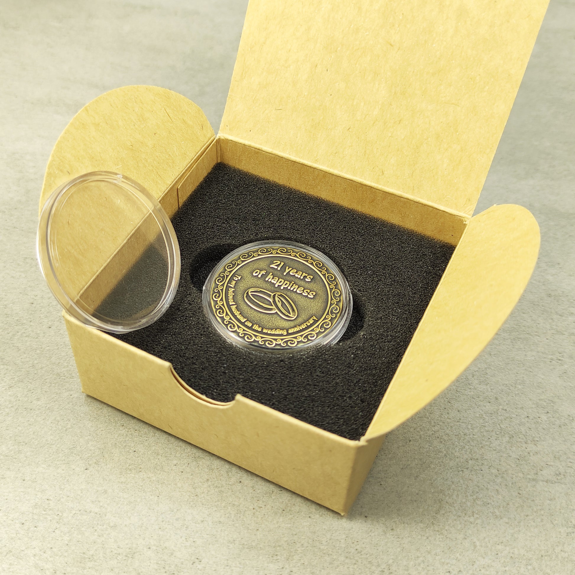 Personalized brass metal coin in a clear acrylic case next to a minimalist eco-friendly gift box for a wedding anniversary present.
