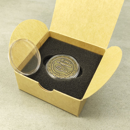 Personalized brass metal coin in a clear acrylic case next to a minimalist eco-friendly gift box for a wedding anniversary present.