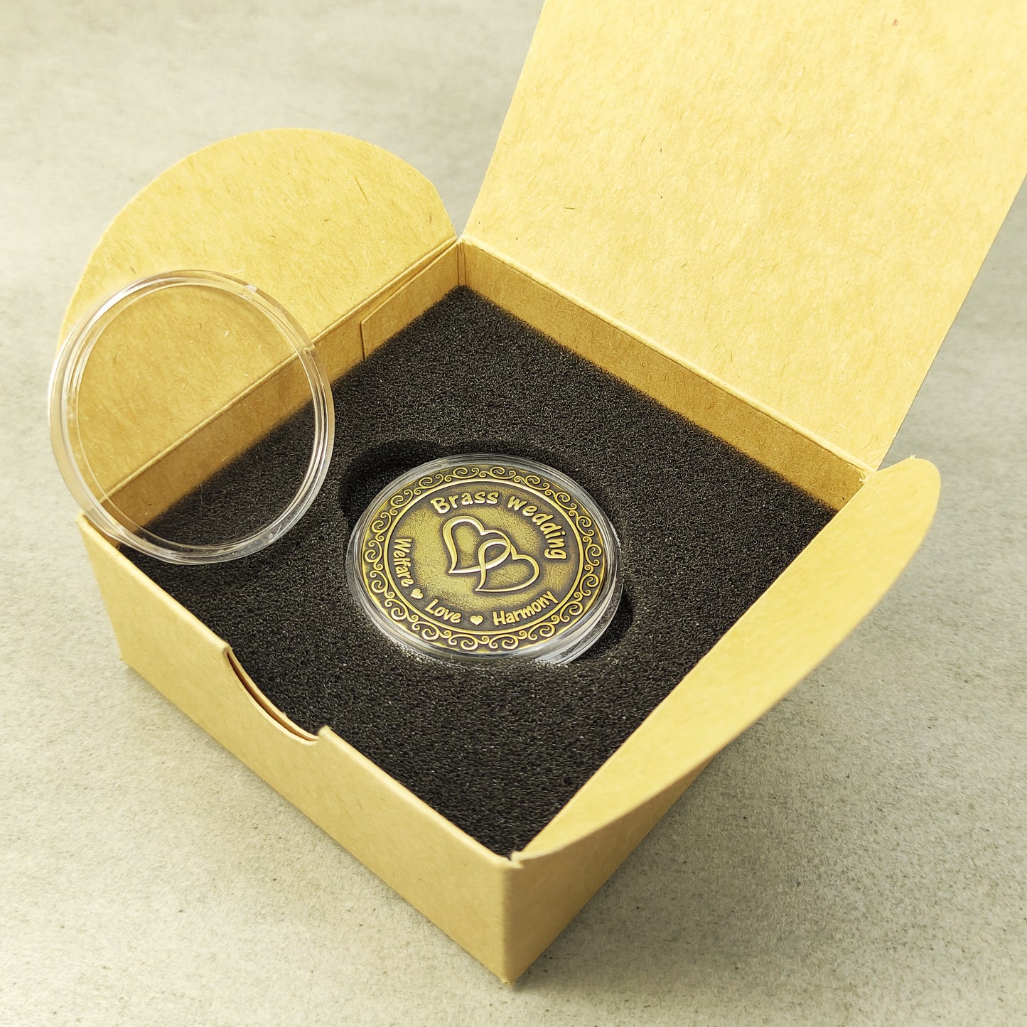 Personalized brass souvenir coin in clear protective case next to a minimalist cardboard gift packaging for wedding anniversary.