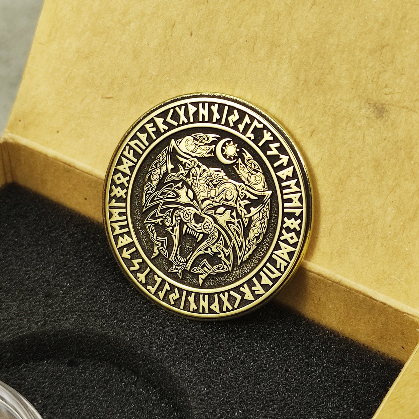 Custom engraved brass Fenrir souvenir coin in a gift box, highlighting the high-contrast black patina and aged brass texture.