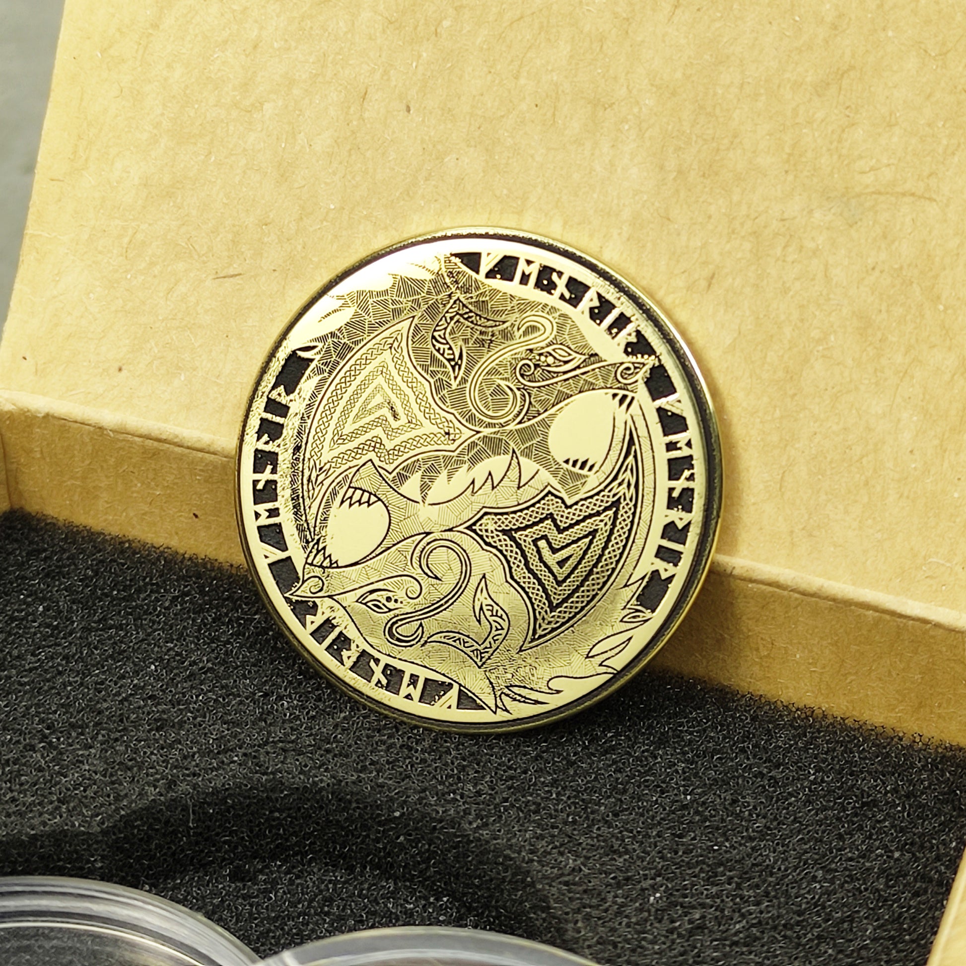 Perspective view of a custom engraved brass Norse coin in a gift box, highlighting the high-contrast engraving and golden highlights.