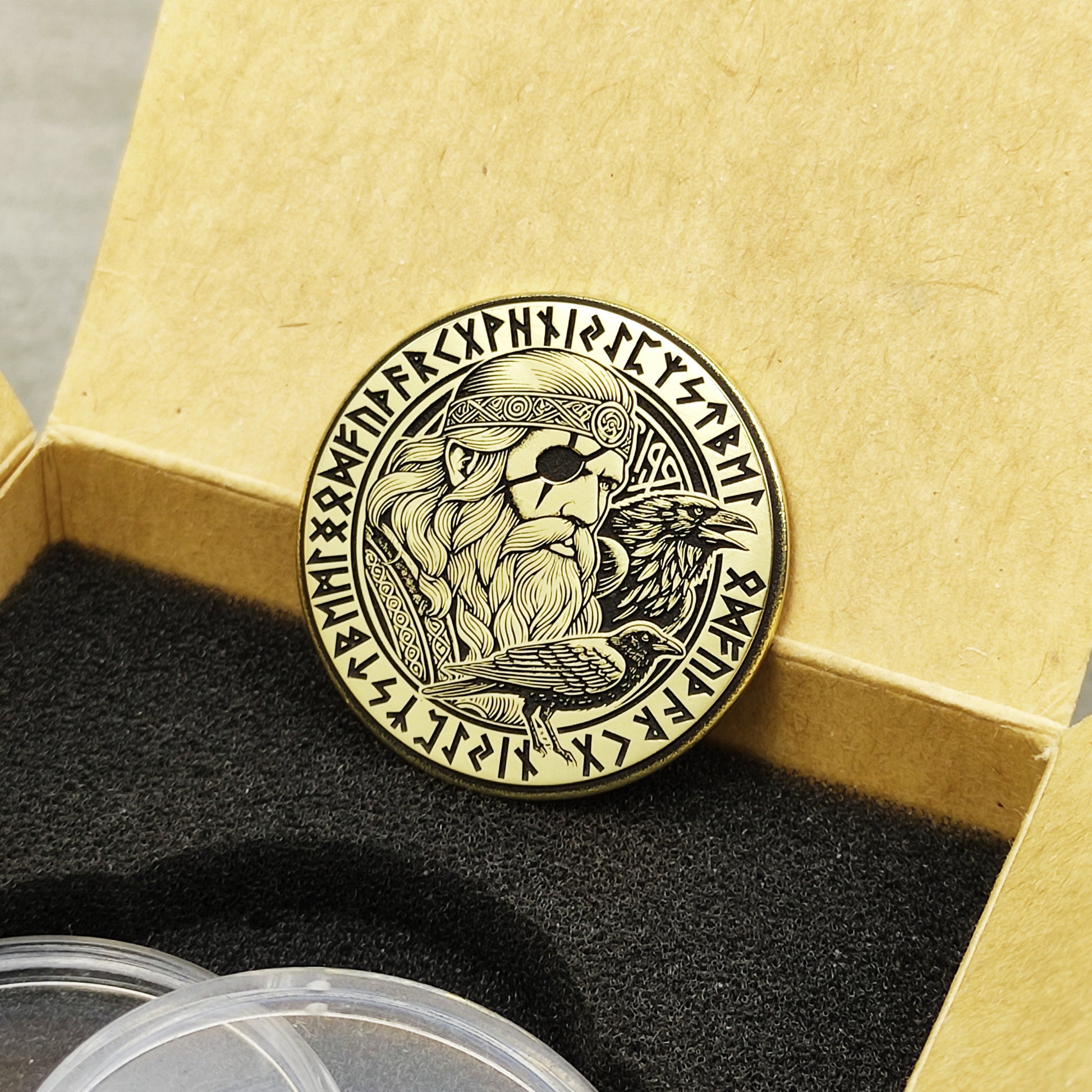 Perspective view of a 2mm thick brass Odin challenge coin in a craft box, showcasing precision etching and aged metal look.