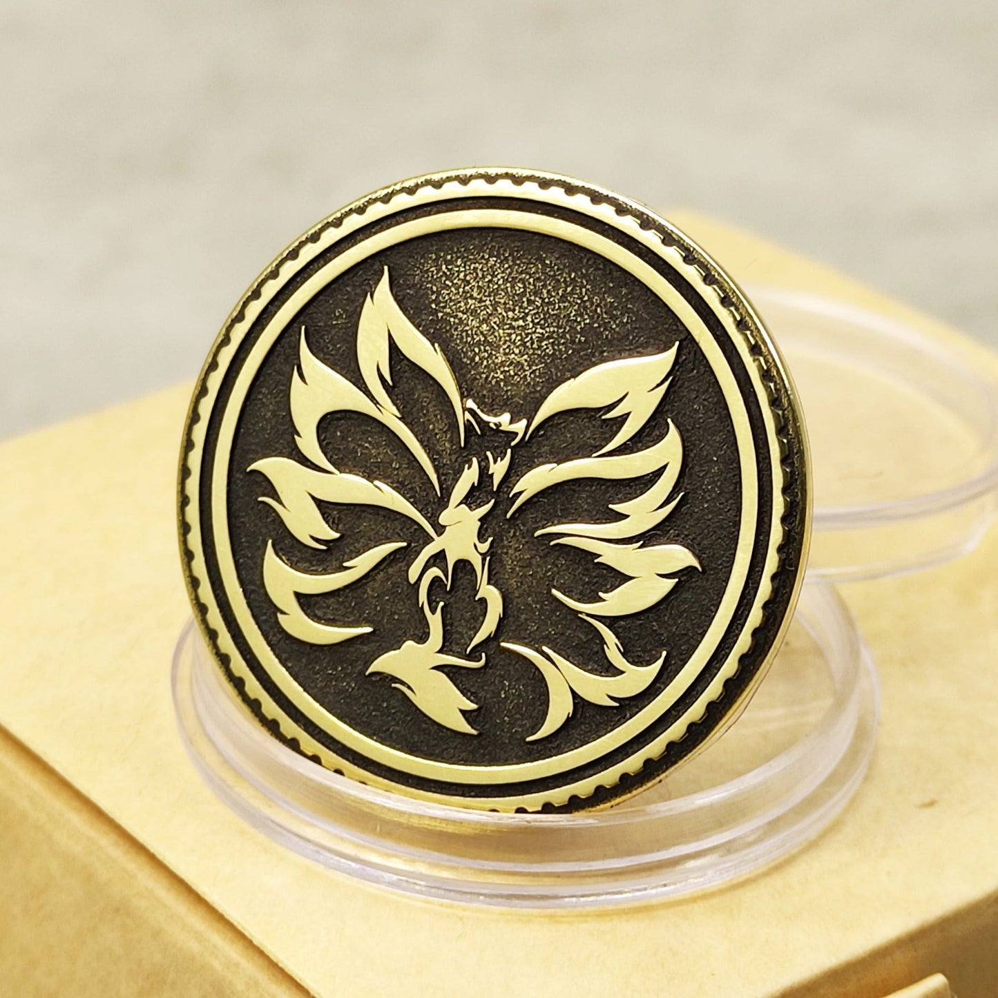 Detailed view of brass Kitsune coin with nine-tailed fox engraving on a clear stand, featuring deep relief and black patina.