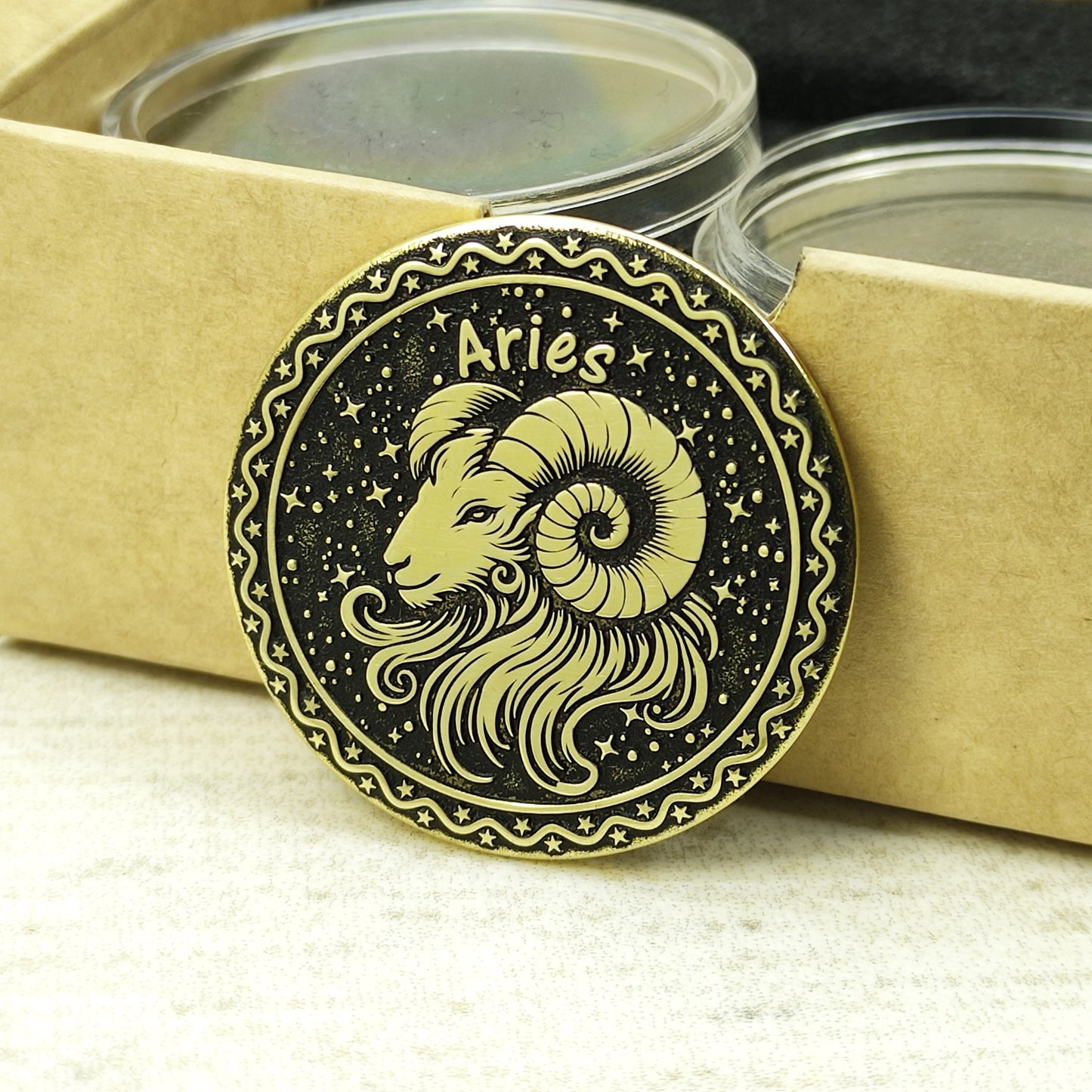 Aries zodiac brass medal leaning against a craft gift box, highlighting the antique gold-tone material and precision laser-etched details.