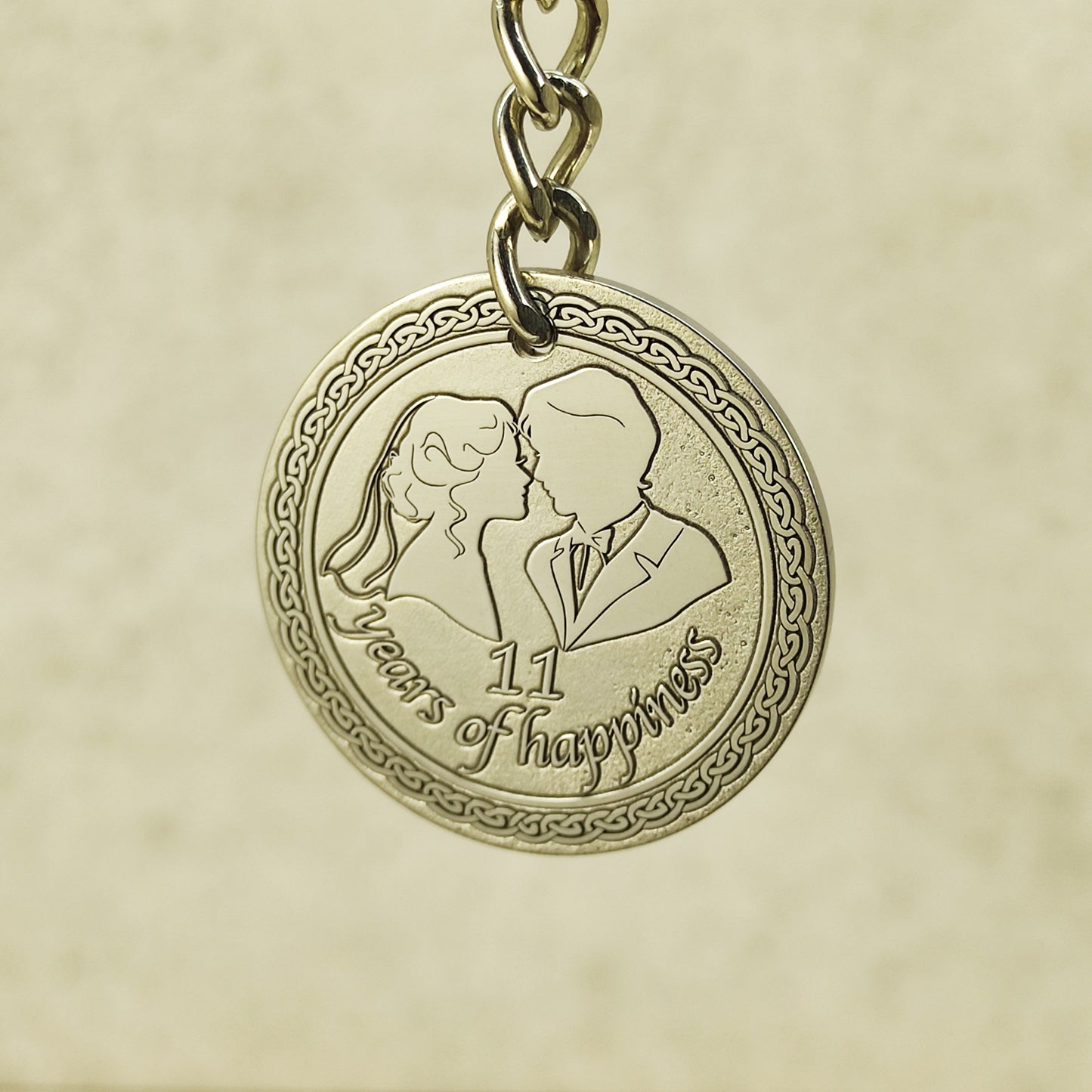 Detailed macro shot of engraved stainless steel coin for 11th anniversary, featuring 3D-style engraving of a husband and wife with decorative celtic border.