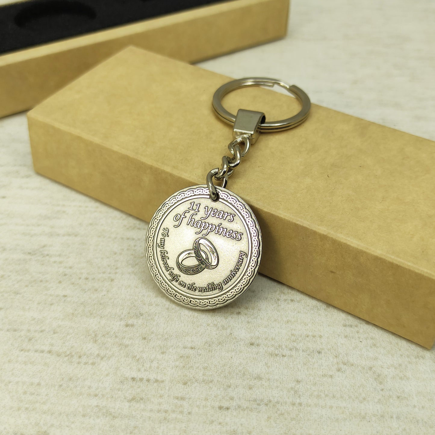 Top view of 11th wedding anniversary brass coin keychain placed next to craft gift packaging, personalized engraved metal souvenir for wife.