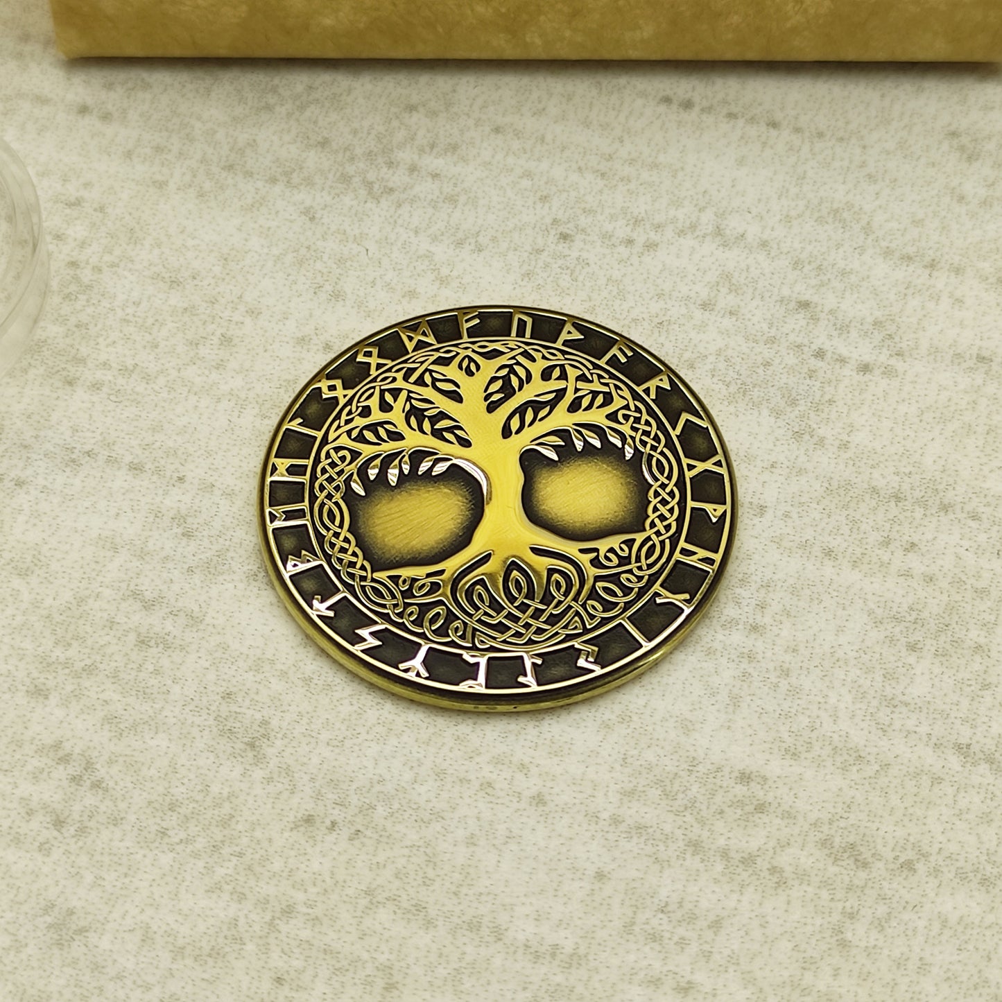 Top view of a brass Yggdrasil amulet coin featuring intricate laser engraving of the Norse World Tree and Elder Futhark runes.