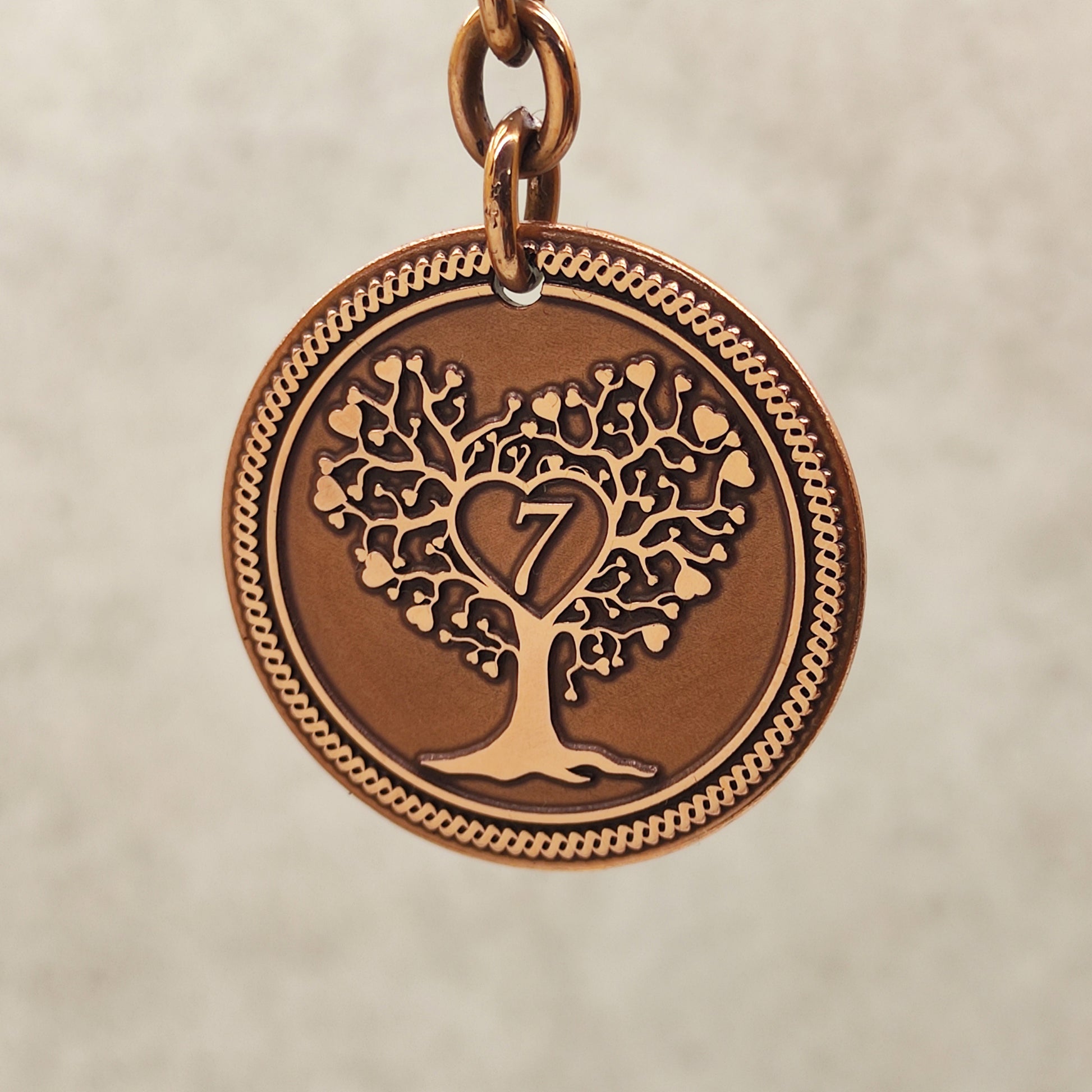 Macro shot of the obverse side of a copper 7 year anniversary coin featuring detailed Tree of Life engraving and decorative border.