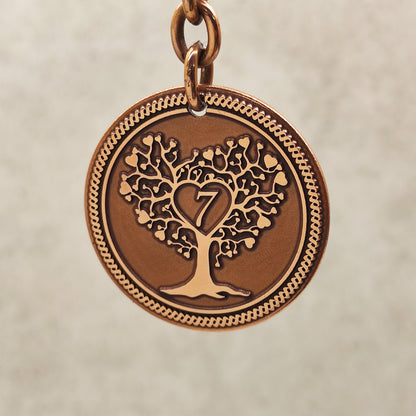 Macro shot of the obverse side of a copper 7 year anniversary coin featuring detailed Tree of Life engraving and decorative border.