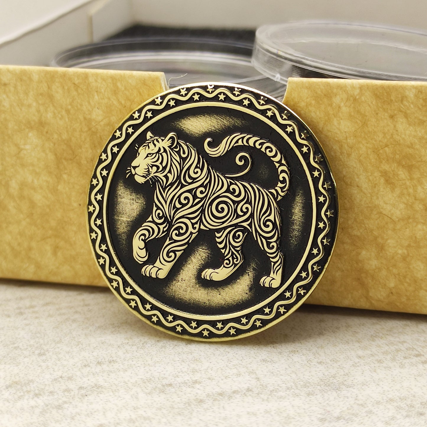Brass Year of the Tiger zodiac coin leaning against an eco-friendly craft gift box, highlighting the polished brass quality and ornamental edge.