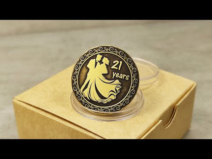 Personalized 21st anniversary brass gift coin in protective capsule next to eco-friendly craft paper gift box.